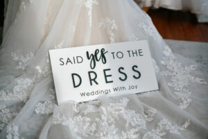 sign saying "Said Yes to the Dress Weddings With Joy" leaned up against bridal gown train