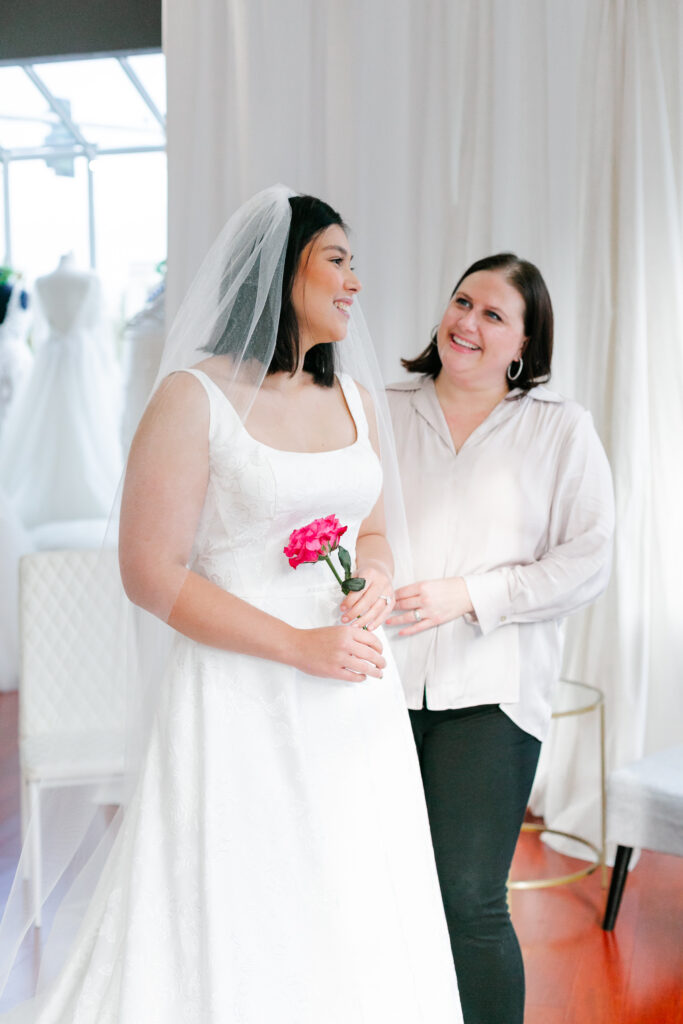 Bridal stylist helps bride try on wedding dress. Weddings with Joy