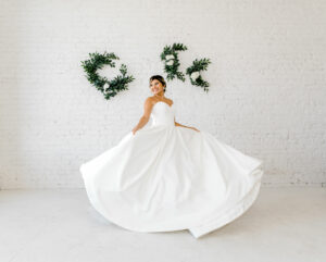 Weddings With Joy bride wearing her wedding gown and twirling in front of a white brick wall.