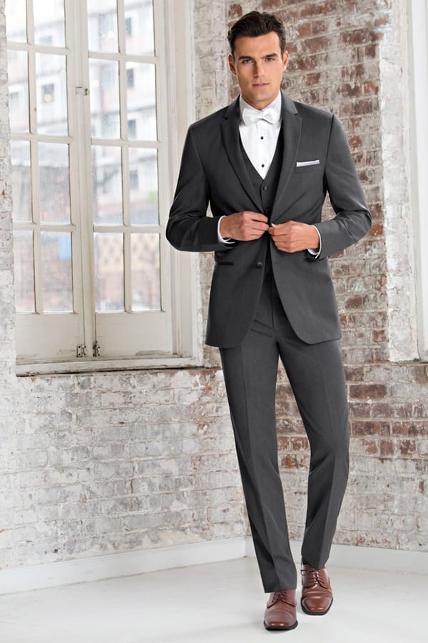 Dashing light grey suit from Weddings with Joy worn by a young man who is buttoning the jacket.