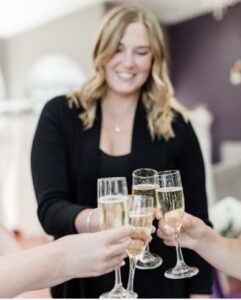 After Hours try on experience at Weddings With Joy. The bridal party and their bridal sylist are cheersing their champagne flutes together.