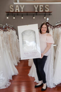 Courtney Foreman, owner of Weddings With Joy, posing with one of her wedding gowns that have been boxed by her Wedding Gown Cleaning And Preservation service.