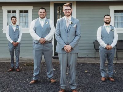 4 groomsmen in formal attire standing in front of house