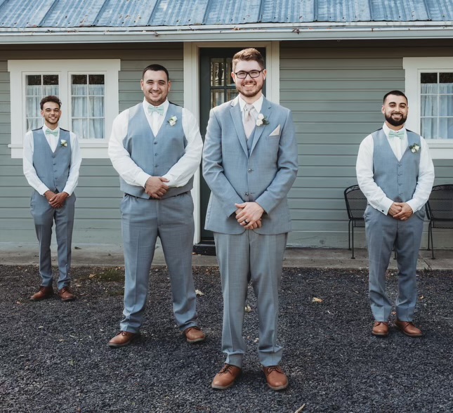 4 groomsmen in formal attire standing in front of house