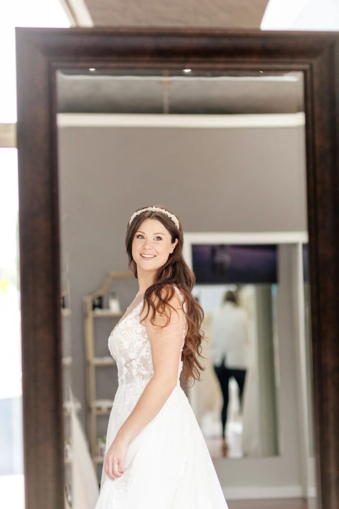 Bride trying on lace bodice wedding dress looks in mirror, crystal bridal hairpiece. Weddings with Joy. 