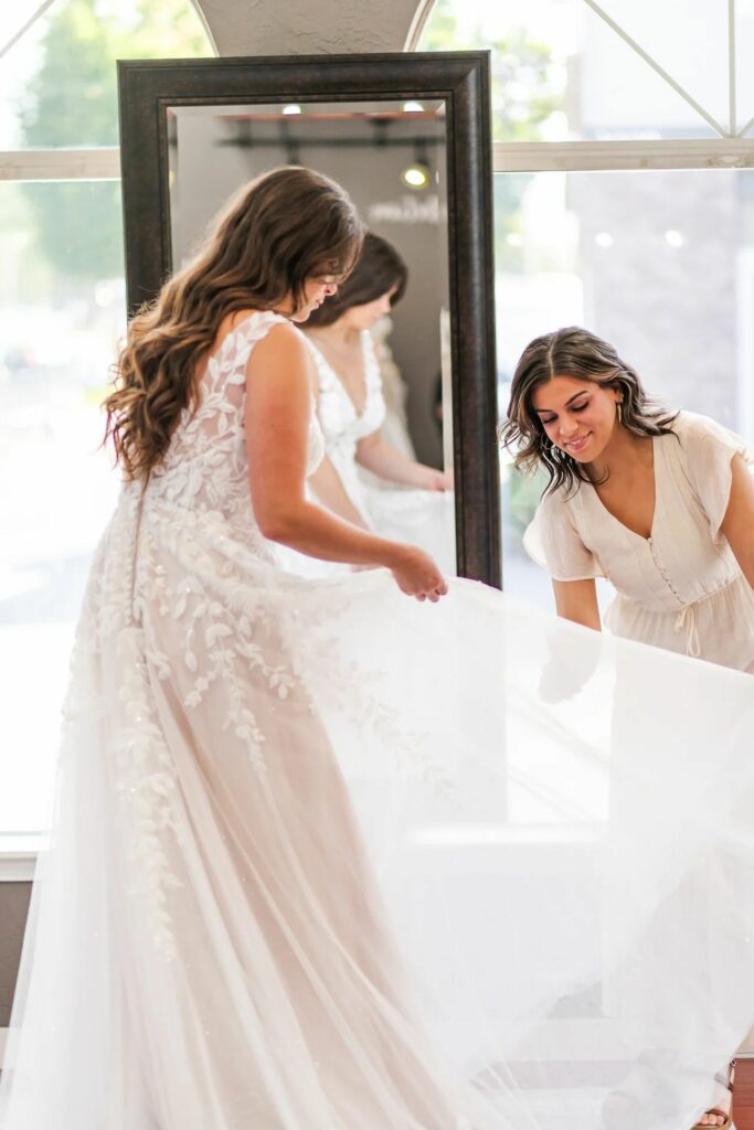 A bride tries on a lace and tulle wedding dress with the help of a bridal consultant. Weddings With Joy.