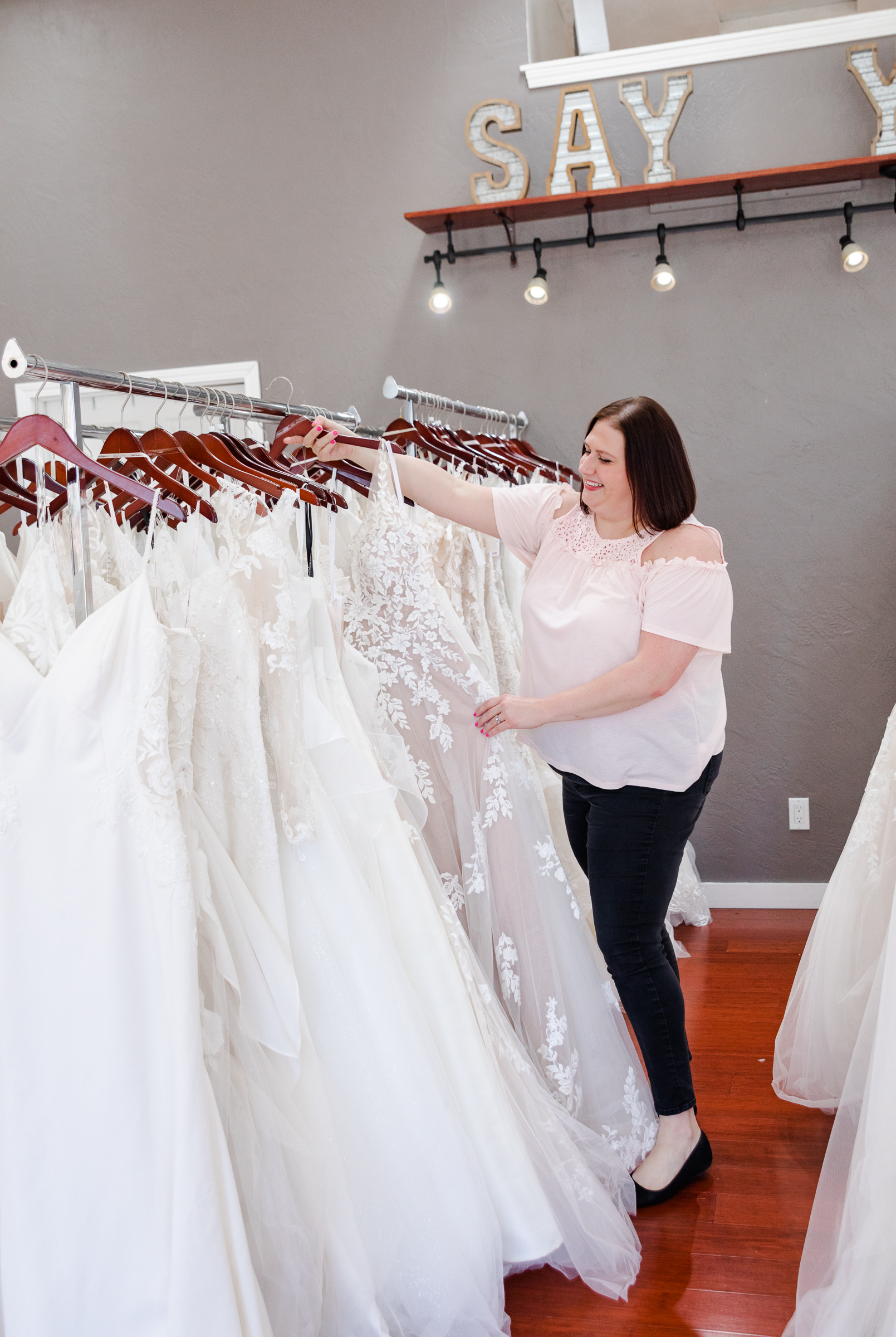 woman looking at wedding dresses on bridal store rack. Weddings with Joy. 