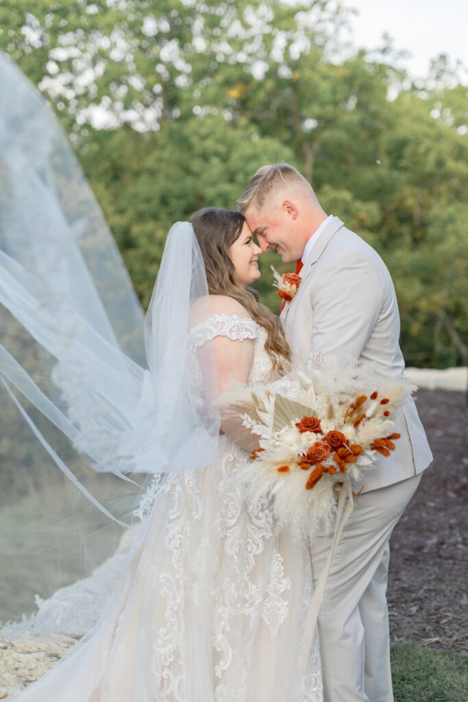 Wedding portrait with flowing bridal veil, bride in lace ball gown wedding dress with off shoulders straps, dried floral boho bridal bouquet. Weddings with Joy. 