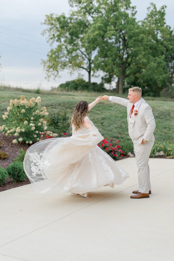 portrait of bride and groom outside dancing, groom twirling bride in lace ball gown with off shoulders straps. Weddings with Joy.