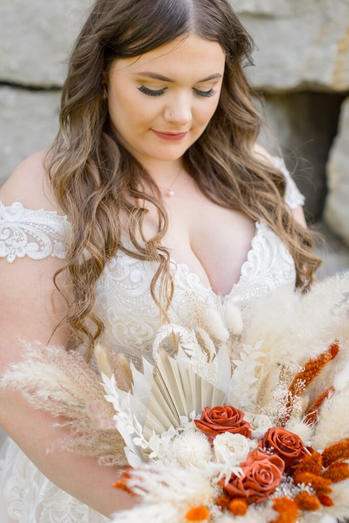 Close up portrait of bride in lace wedding dress with off the shoulders straps and dried floral boho bridal bouquet. Weddings with Joy. 