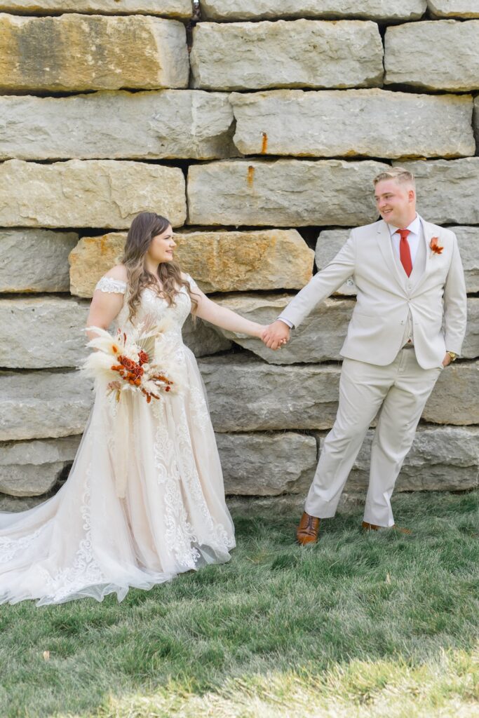 plus size bride in lace ball gown with long train and off shoulders straps, groom in tan suit with burnt orange tie. dried floral boho bridal bouquet. Weddings with Joy.