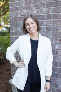 Bridal Stylist from Weddings with Joy, Austyn. She has short brown hair and is wearing a black outfit with a white sport jacket.