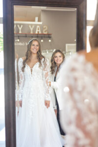 Hannah, a Weddings with Joy bridal stylist, helping a bride to be select her wedding dress with long sleeves.