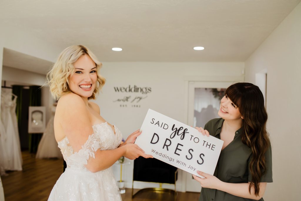 Happy bride and bridal stylist holding sign saying "Said yes to the dress"
