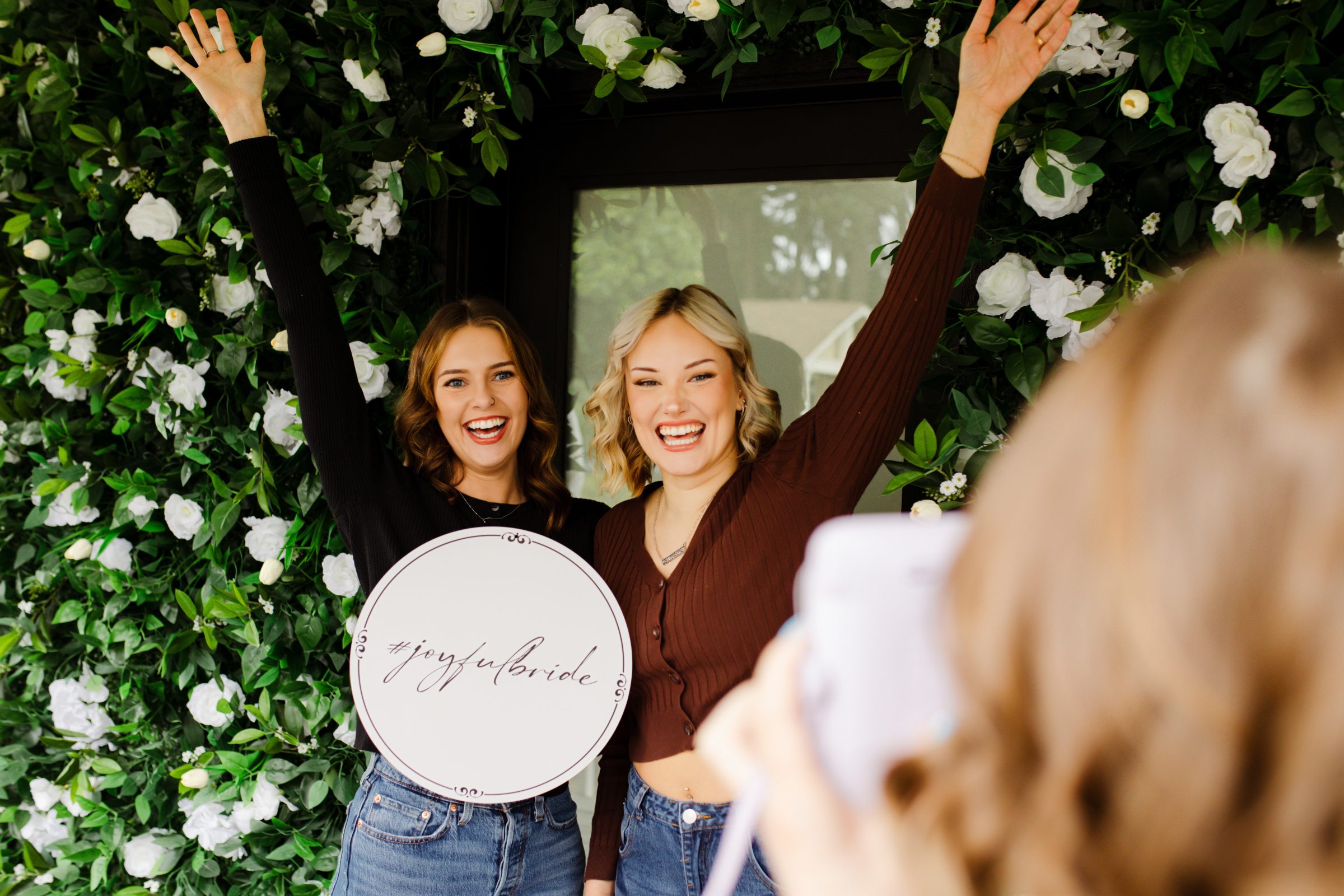 two happy women celebrating taking a picture in front of floral wall
