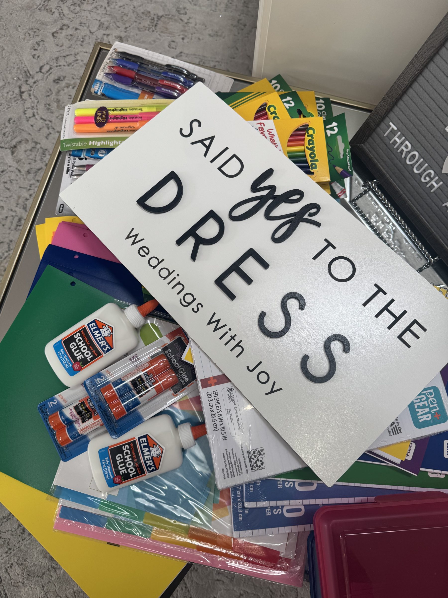 Weddings with Joy sign on top of pile of school supplies